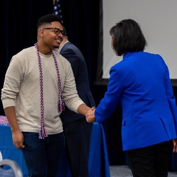 President Mantella shaking hands with a student veteran wearing his cords.